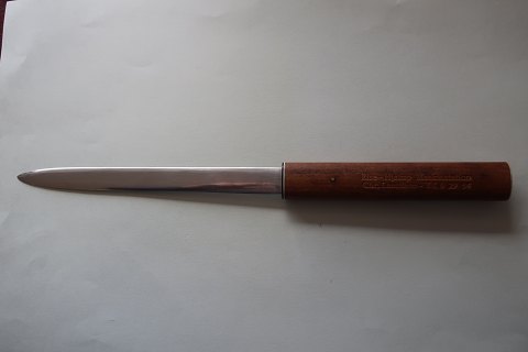 An old paper knife/paper cutter with a handle made of wood
The handle is with text for advertising with name
Text: "Rise Hjaruo Maskinstation, Chr. Lauritsen, Tlf.: 6 29 54", Denmark
The blade of the knife is with the words: "tainless Steel" and so mad