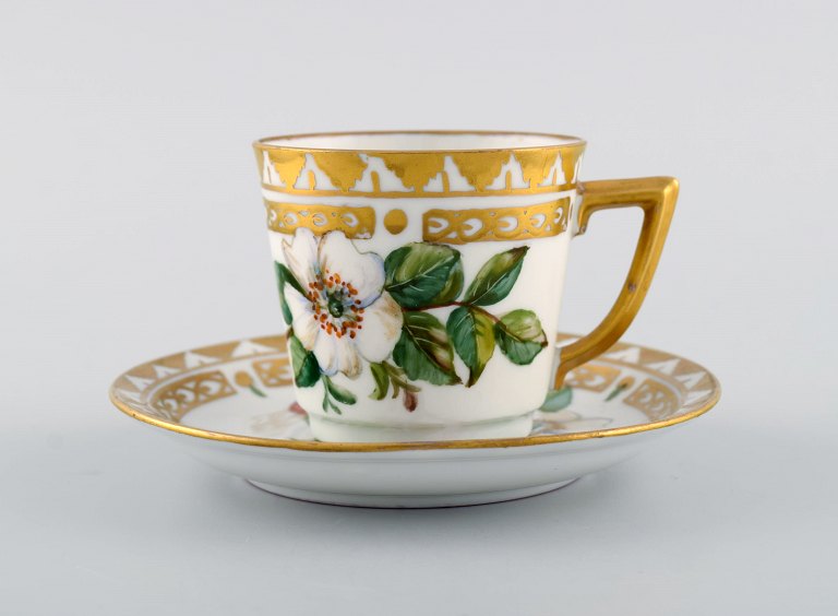 Royal Copenhagen kaffekop med underkop i håndmalet porcelæn med gulddekoration 
og blomster. Flora danica stil, 1960