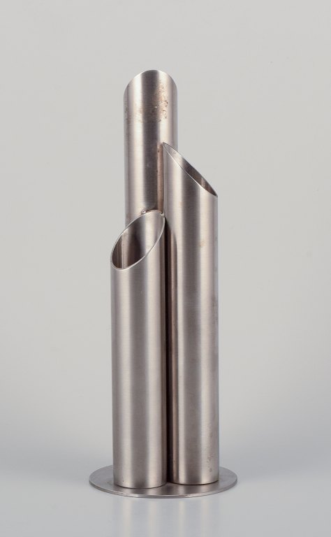 Swedish industrial designer. 
Stainless steel vase designed with three interconnected tubes on a round base. 
Brutalist style.